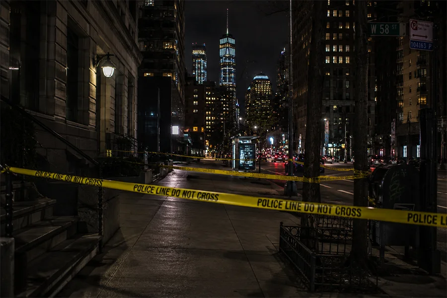Yellow police line tape across a Manhattan sidewalk at night with tall buildings behind