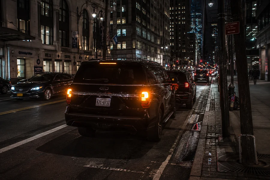 Dark SUV double-parked on a New York City street at night with emergency lights on