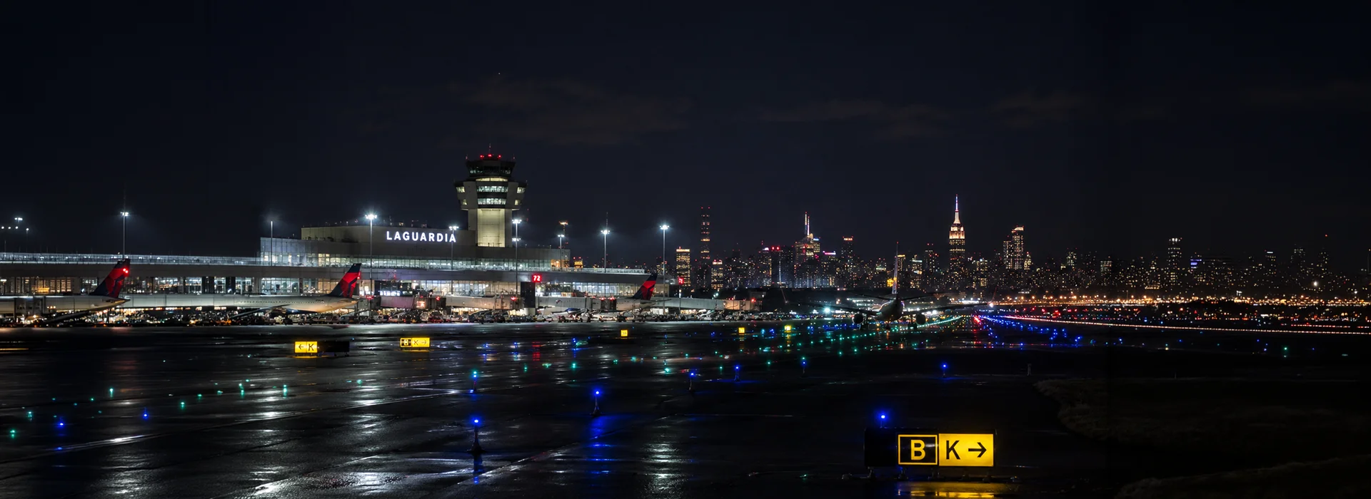 LaGuardia Airport at night with an illuminated runway and the Manhattan skyline behind