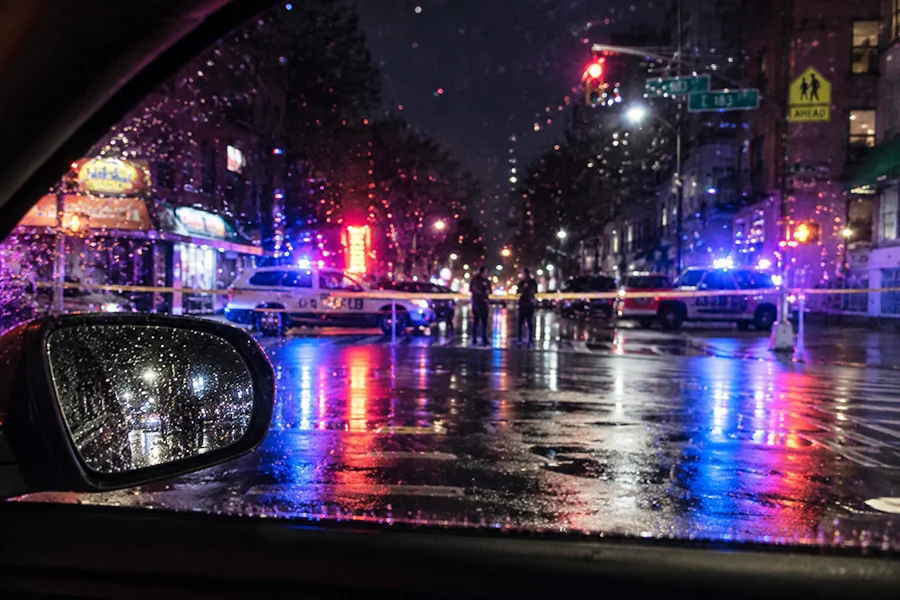Cordoned-off scene with blue and red police lights seen through a rain-covered vehicle window in New York